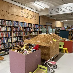 Speelgoedafdeling met boekenkast, speelgoed in grote dozen en kinderspeelgoed op de winkelvloer