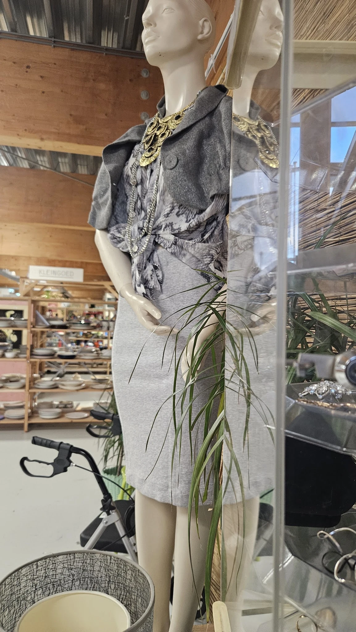 Winkelinterieur met etalagepop, hangende plant en stellingen met servies op de achtergrond