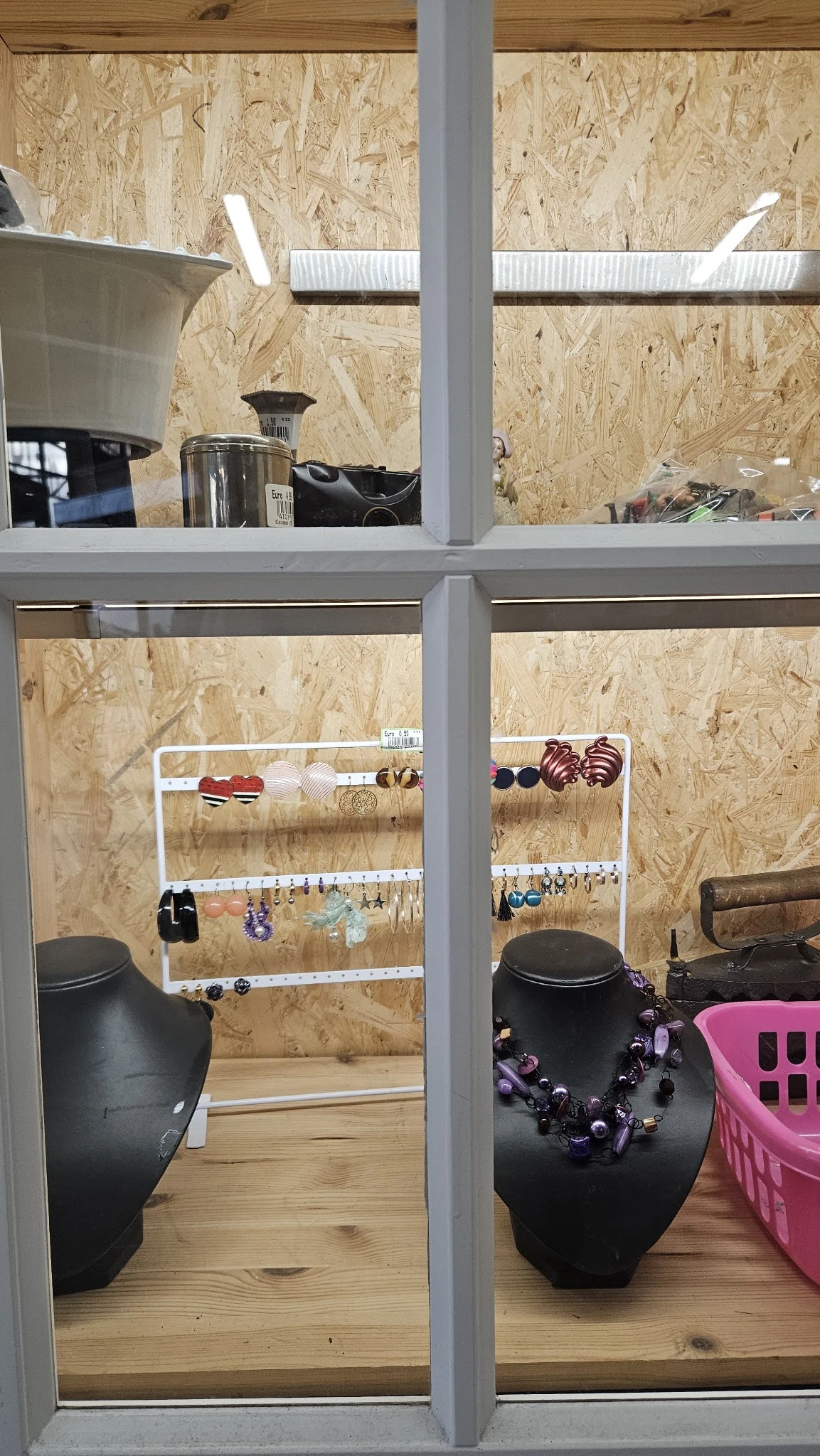 Witte metalen rekken met uitgestalde sieraden, armbanden en accessoires tegen een MDF-wand