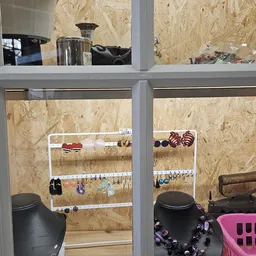 Witte metalen rekken met uitgestalde sieraden, armbanden en accessoires tegen een MDF-wand