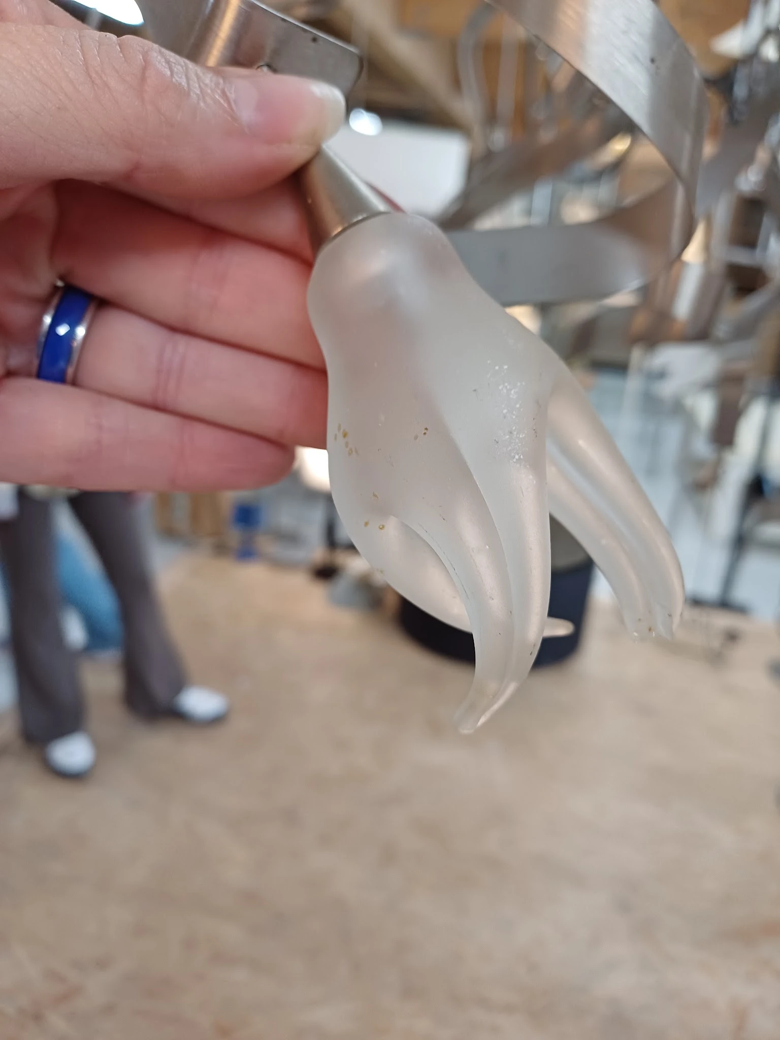 Close-up van een wit porselein decoratief object met gebogen vormen, gehouden in een hand met blauwe ring