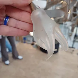 Close-up van een wit porselein decoratief object met gebogen vormen, gehouden in een hand met blauwe ring