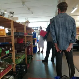 Binnenkant van kringloopwinkel met houten stellingen vol spullen en bezoekers aan het winkelen