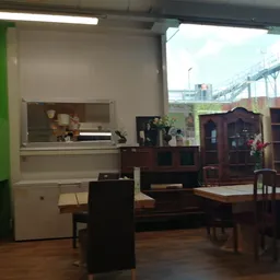 Winkelvloer met tweedehandsmeubels: kasten, tafels en stoelen, groene muur met keukenunit links