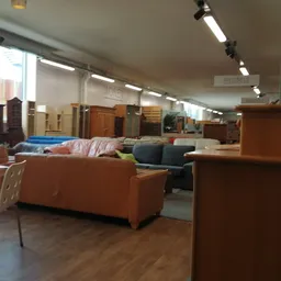 Winkelvloer met diverse meubels waaronder oranje en blauwe banken, kasten en stoelen in een grote ruimte met helder licht