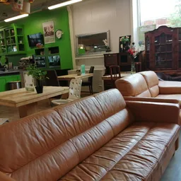 Bruine leren banken en zitmeubels in een kringloopwinkel met groene muur en houten tafels op de achtergrond