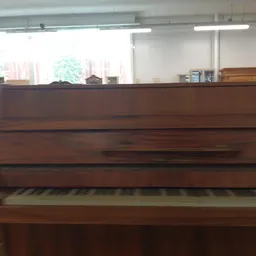 Bruine houten piano met toetsen zichtbaar, in een winkelruimte met grote ramen
