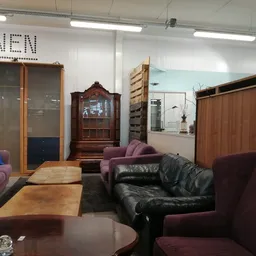 Woonkamer ingericht met diverse meubels: paarse en zwarte fauteuils, houten kasten, bijzettafels en decoratie