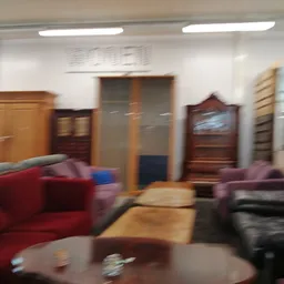 Woonkamer met rode en paarse stoelen, houten kasten en salontafel in kringloopwinkel