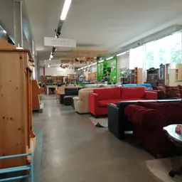 Winkelvloer met rode en donkere banken en zitmeubels, houten kasten links, natuurlijke verlichting van ramen