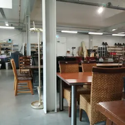 Winkelvloer met houten tafels, stoelen en stellingen met spullen in een kringloopwinkel