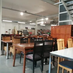 Winkelvloer met diverse tweedehands meubels: houten stoelen, tafels, kasten en een trap op de achtergrond