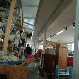 Binnenkant van kringloopwinkel met stellingen, kasten, hangende items en bezoekers lopend door het gangpad