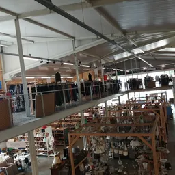 Overzicht van de kringloopwinkel met twee niveaus: bovenverdieping met kleding en rekken, benedenverdieping met huishoudelijk