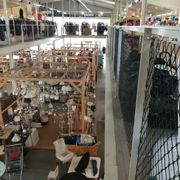 Overzicht van kringloopwinkel met houten stellingen vol spullen, twee verdiepingen zichtbaar met kleding en huishoudartikelen