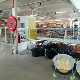 Winkelvloer met stellingen, een rode brandblusser aan de muur, en vooraan zwarte tassen en blauwe kinderspeelartikelen