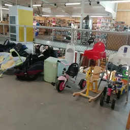 Speelgoed en kindervoertuigen in de kringloopwinkel, waaronder driewielers, een rode piano en diverse speelartikelen