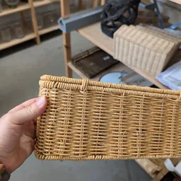 Hand met armband houdt een rechthoekig rieten mandje vast