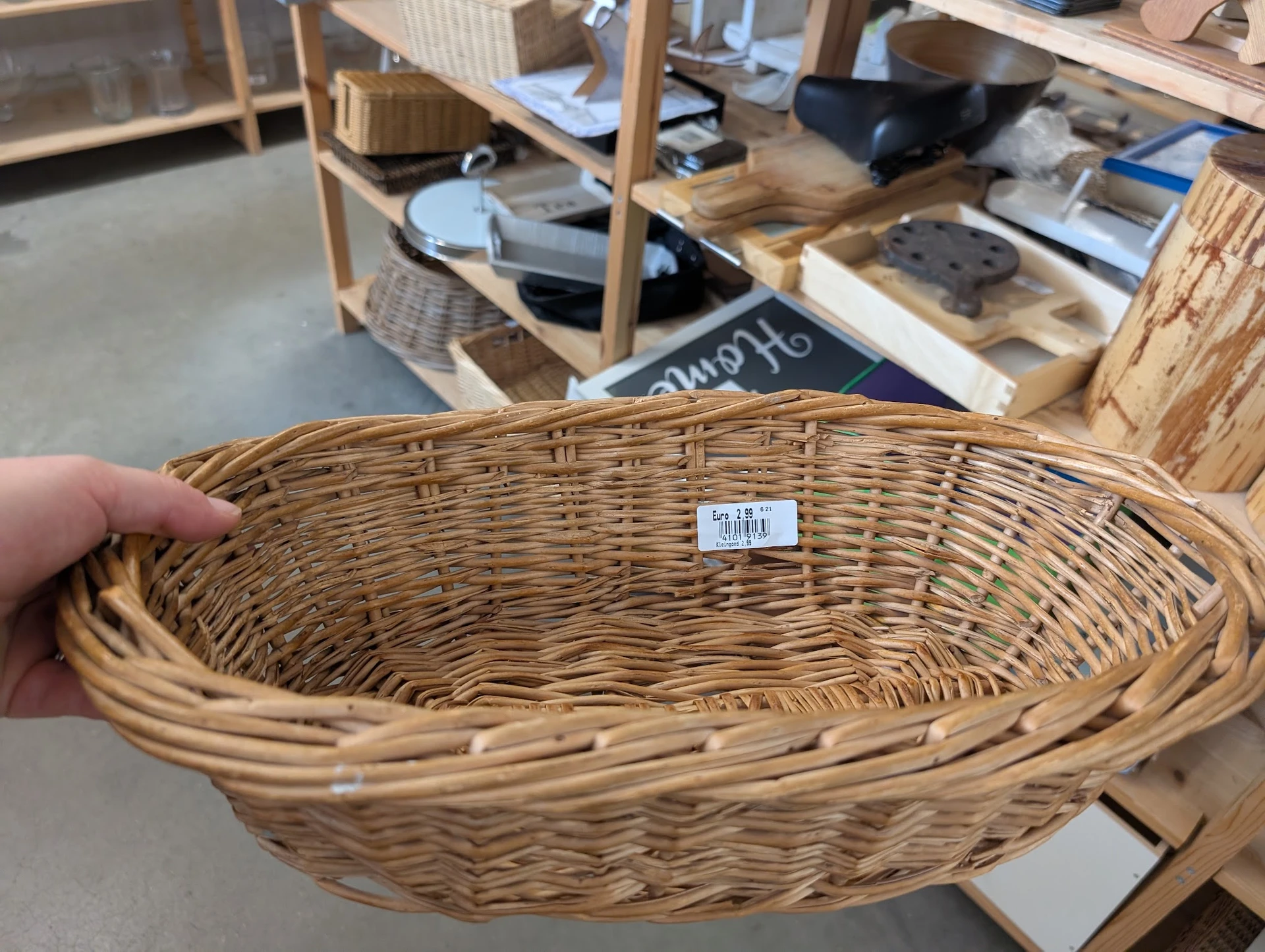 Ovale rieten mand met prijskaartje, gehouden in een hand in een kringloopwinkel