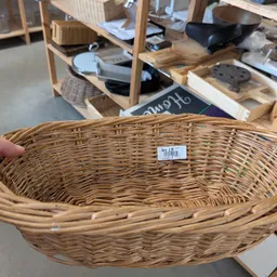 Ovale rieten mand met prijskaartje, gehouden in een hand in een kringloopwinkel