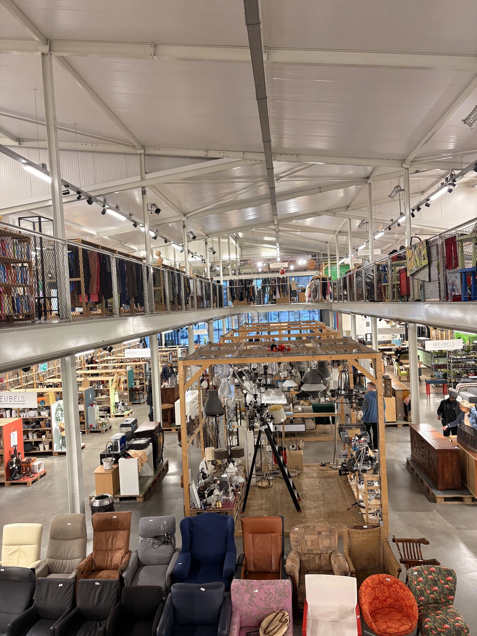 Ruim interieur van kringloopwinkel met twee verdiepingen, stellingen met kleding, toonbanken en diverse goederen zichtbaar