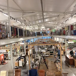 Ruim interieur van kringloopwinkel met twee verdiepingen, stellingen met kleding, toonbanken en diverse goederen zichtbaar