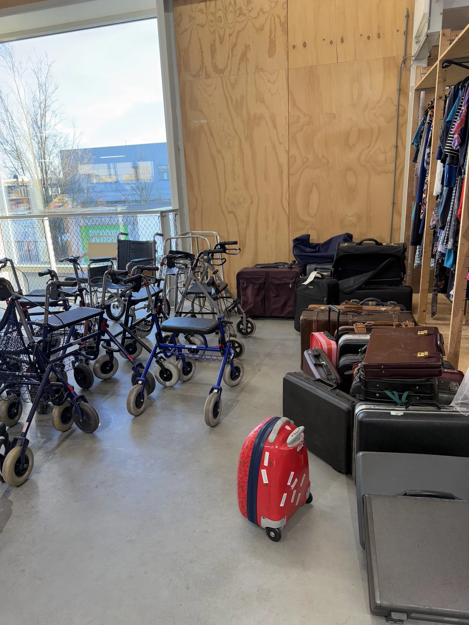 Winkelvloer met rollatoren, wandelhulpen en koffers, kleding aan rekken op de achtergrond