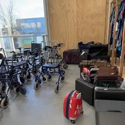 Winkelvloer met rollatoren, wandelhulpen en koffers, kleding aan rekken op de achtergrond