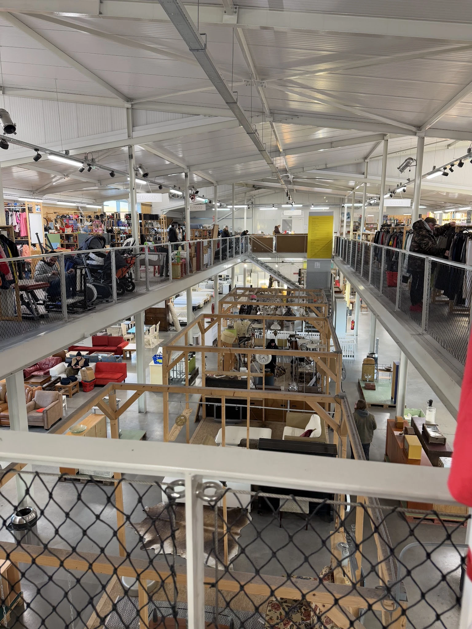 Overzicht van twee etages in een kringloopwinkel met verschillende afdelingen, stellingen en merchandise