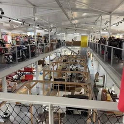 Overzicht van twee etages in een kringloopwinkel met verschillende afdelingen, stellingen en merchandise