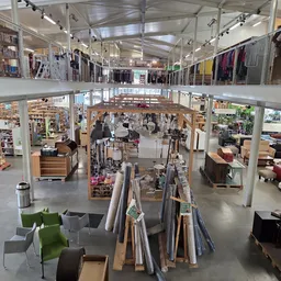 Overzicht van de winkelvloer met stellingen, afdelingen en bezoekers in een kringloopwinkel met twee verdiepingen