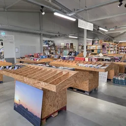 Winkelvloer van kringloopwinkel met houten stellingen vol boeken en spullen, heldere verlichting