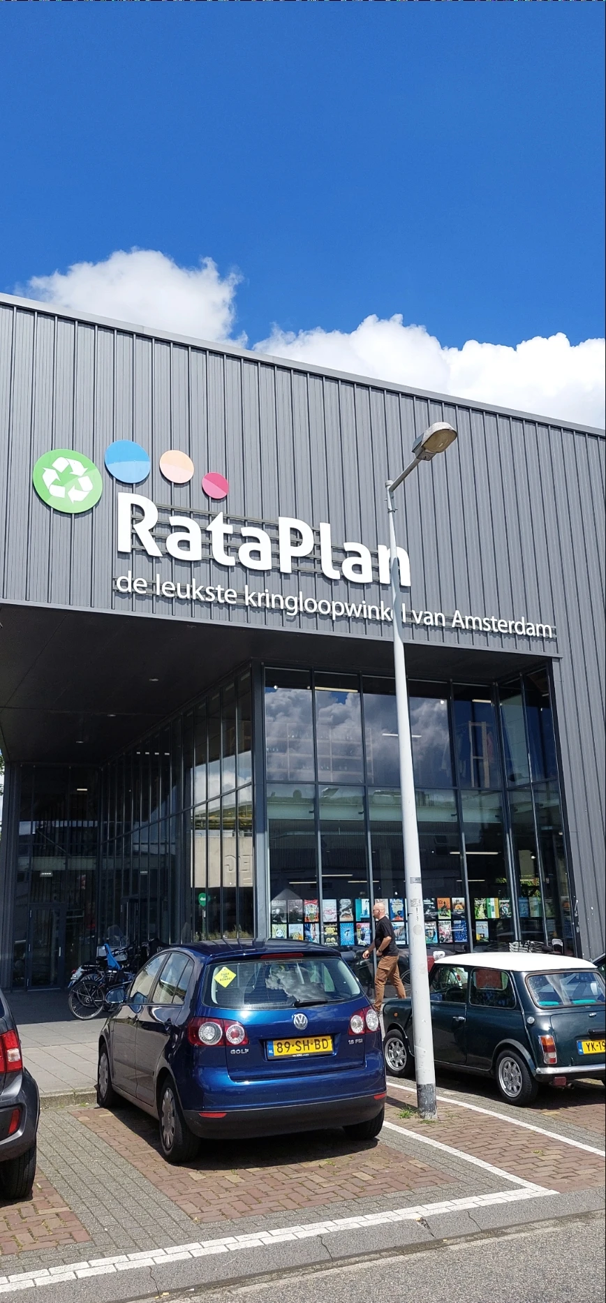 Gevel van kringloopwinkel RataPlan met wit logo en winkelraam op grijze metalen wand