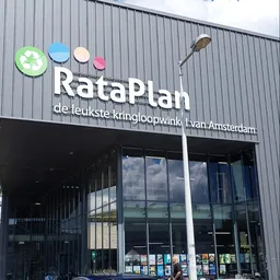 Gevel van kringloopwinkel RataPlan met wit logo en winkelraam op grijze metalen wand
