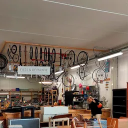Werkplaats met fietsen aan wandrek en montage-werkstation, bord 'FIETS & REPARATIE' zichtbaar