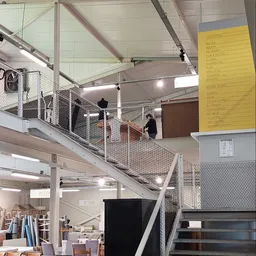 Bovenaanzicht van de winkelvloer met metalen trap, reling en netwerk, stellingen met spullen, gele prijskaart aan muur