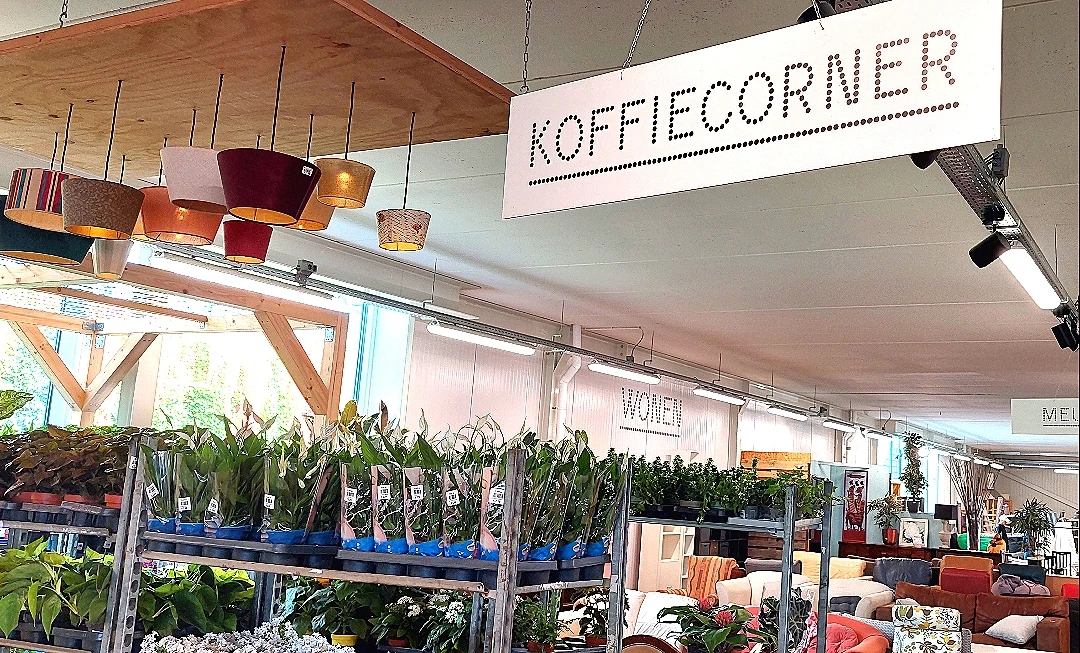 Koffiehoek met naam 'Koffiecorner' boven aan de wand, met blauwe plantenbakken en hangende lampen