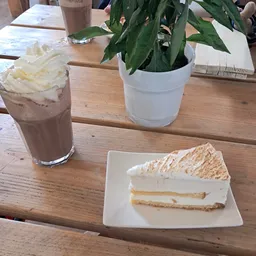 Tafel met een stuk cake met slagroom, een glas chocolademelk met slagroom, een potplant en notitieboekje