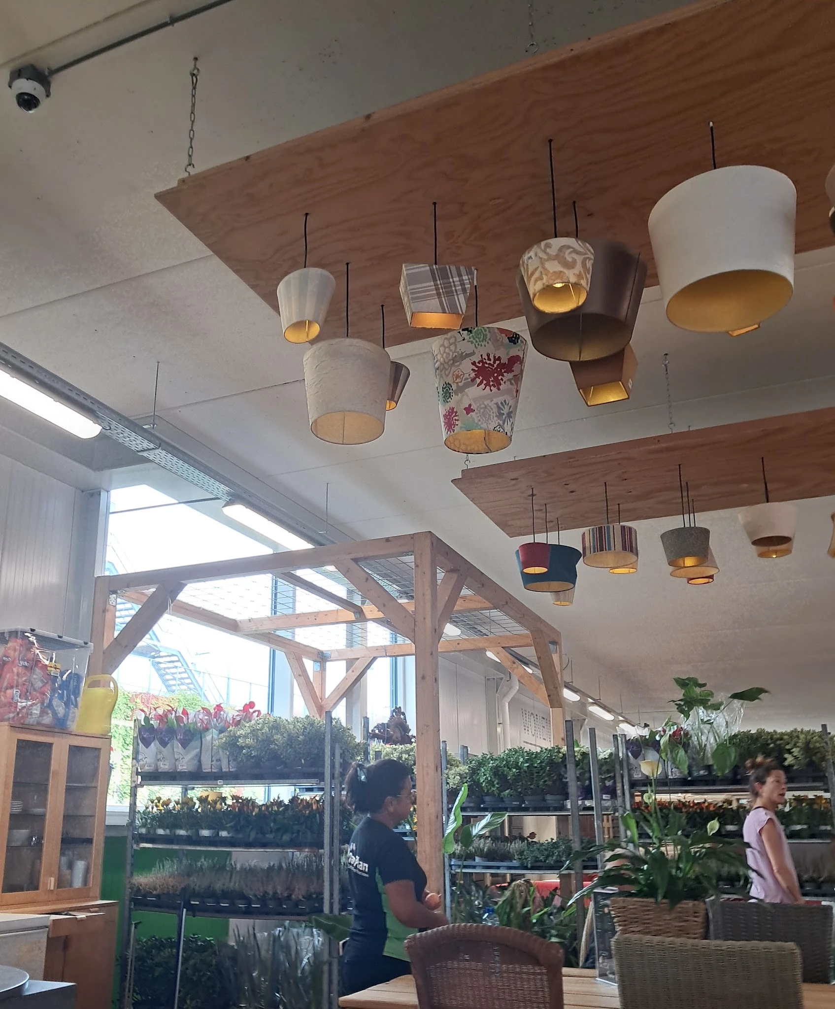 Interieur van winkel met houten balken, hangende design-lampen en uitzicht op planten en winkelruimte