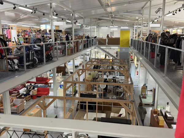 Overzicht van tweelaagse kringloopwinkel met rekken kleding boven en houten displays beneden