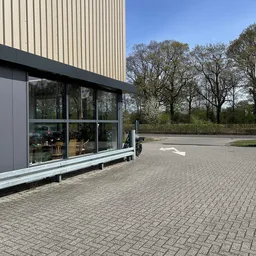 Moderne gevel van kringloopwinkel met grote raampartijen, terras en parkeerplaats