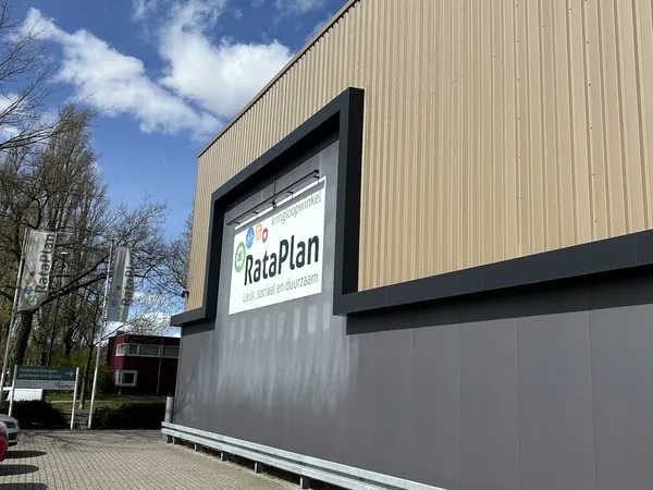 Gevel van kringloopwinkel RataPlan met verlicht logo en grijze pui aan Kanaal Zuid