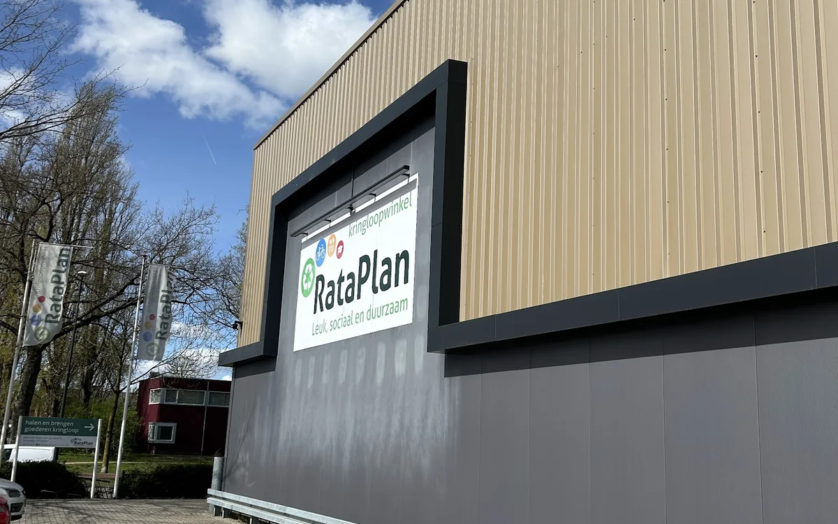 Gevel van kringloopwinkel RataPlan met verlicht logo en grijze pui aan Kanaal Zuid