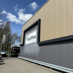 Gevel van kringloopwinkel RataPlan met verlicht logo en grijze pui aan Kanaal Zuid