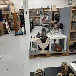 Uitgestalde tweedehands huishoudartikelen en decoratie op tafel in de winkel, waaronder glazen, vazen en vintage tassen