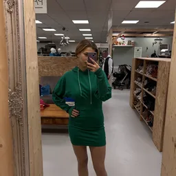 Persoon in groene hoodie neemt selfie in kringloopwinkel