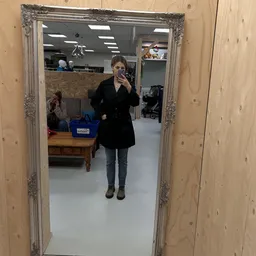 Vrouw met telefoon in kringloopwinkel met houten meubel en blauwe bakken op achtergrond