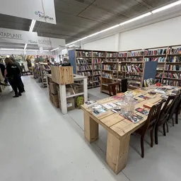 Winkelvloer met boekenkasten, houten tafels met uitgestalde boeken en tijdschriften, één bezoeker zichtbaar