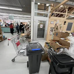 Winkelinterieur met winkelwagen, afvalbakken en kartonnen dozen, ingang en toonbank op achtergrond