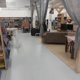 Winkelinterieur met boekenrekken links, grijze gordijnen, bruine bank en houten tafel met stoelen op houten vloer